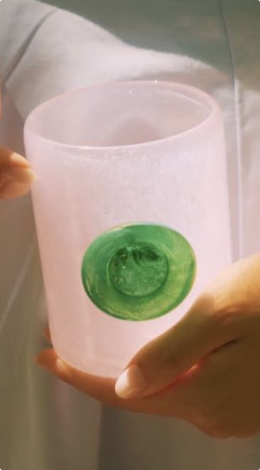 A pink frosted glass with a green seal held in two hands
